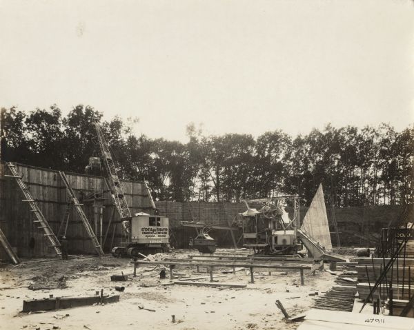 A building site with "O'Dea and Shafer, Engineers and Contractors" construction crew, crane and other equipment. On the photograph album binding on the left side of the photograph is written "Reservoir at Madison" and "Thomas O'Dea's, 'Shadow' Shafer, Building Reservoir in Madison, Wi."