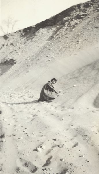 A woman, Grace, digs in the sand as she kneels in a sand pit near the intersection of Fish Hatchery Road and Park Street. A note on the back of the photograph reads, "Pieh's Hill, Keyes Hill."