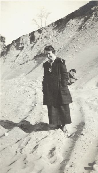 Florance Trask poses standing in a sand pit located near the intersection of Fish Hatchery Road and Park Street. Another woman, Grace, can be seen digging in the sand behind her. A note on the back of the photograph reads, "Pieh's Hill, Keyes Hill."