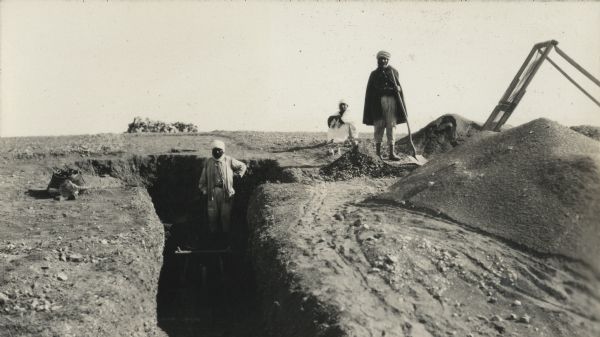 Men excavating a trench in the escargotiere (snail midden) at Medfoun. Brahim is in the trench and Shabane is standing with the shovel. A screen and piles of diggings are on the right. A third man is sitting in the background.