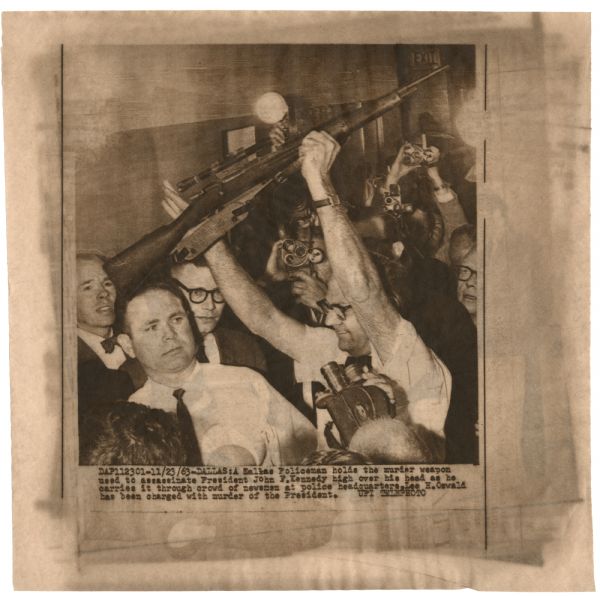 Original UPI Wirephoto transmission. Caption reads: "A Dallas Policeman holds the murder weapon used to assassinate President John F. Kennedy high over his head as he carries it through crowd of newsmen at police headquarters. Lee H. Oswald has been charged with murder of the President."