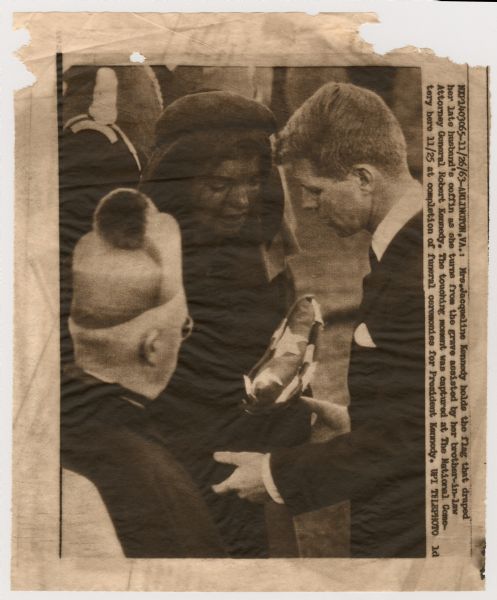 Original UPI Wirephoto transmission. Caption reads: "Mrs. Jacqueline Kennedy holds the flag that draped her late husband's coffin as she turns from the grave assissted by her brother-in-law Attorney General Robert Kennedy. The touching moment was captured at The National Cemetery here 11/25 at completion of funeral ceremonies for President Kennedy."