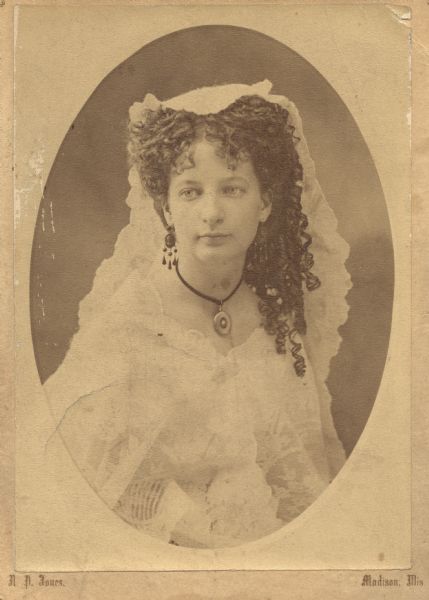 Mrs. Robert B. (Alice Russell Hobbins) Porter posing for a waist-up formal portrait. She is wearing a light-colored lace dress with a lace headpiece. She is wearing a circular pendant on a dark ribbon choker and dark chandelier earrings. Her hair is curled into ringlets.<p>Alice Russell (Hobbins) Porter (1853-1926) was born February 9, 1853 in Wednesbury, Staffordshire, England, the daughter of Joseph Hobbins (1816-1894) and Sarah Badger-Jackson (1816-1870). She moved to Madison, Wisconsin with her family in 1854. On March 7, 1884 she married Robert Percival Porter (1852-1917) in Madison. Alice began her career as a journalist in 1877, when she began working as a correspondent for several newspapers including the Milwaukee Sentinel and <i>Wisconsin State Journal</i> with her base in Chicago. She also was a staff member of the <i>Chicago Daily Inter-Ocean</i> newspaper. In 1879 she moved to New York and worked as a correspondent for several western newspapers and New York papers. Before her marriage she visited Europe twice as a correspondent and must have worn this bodice on one of those trips. Supposedly she was the first female reporter sent to Paris as a newspaper correspondent. Porter was also a journalist. Born in England he moved to Chicago, where he worked for the US government as a census worker and on the tariff commission. He also worked for the Inter-Ocean. In 1887 he founded the <i>New York Press</i>, for which Alice wrote several articles. Her main interest was women's and children's welfare. Porter died in an automobile accident while working for the <i>London Times</i>.