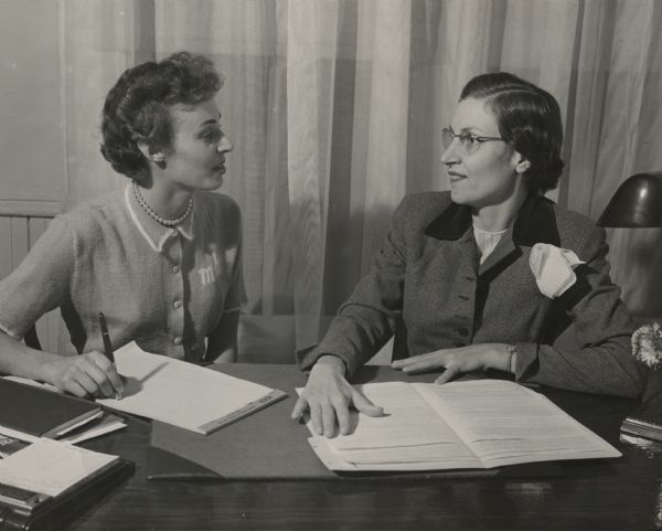Mary Herb (left), the Wisconsin State Student Nursing Association President and Signe Skott Cooper (right), Wisconsin State Student Nursing Association Advisor, have a conversation while seated together behind a desk.