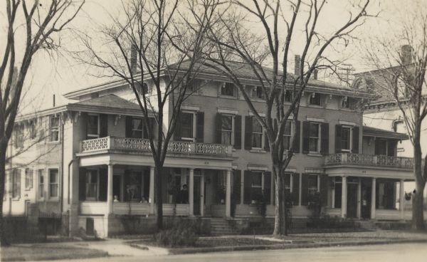 View across street towards house at 210 Monona Avenue (now Martin Luther King, Jr. Boulevard), a property owned by Colonel George M. Neckerman and Elizabeth Shwab Neckerman. George was a dry goods merchant and Elizabeth was the first kindergarten teacher in Madison. Three people are posed on the porch.