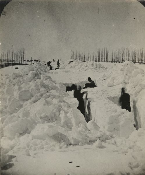 Winter scene with men digging out the train tracks by hand after a big snow storm. Trees and a fence line the sides of the railroad right of way. Between February 27th and March 4th, 1881, 2 to 4 feet fell in eastern and central Wisconsin with drifts up to 20 feet.