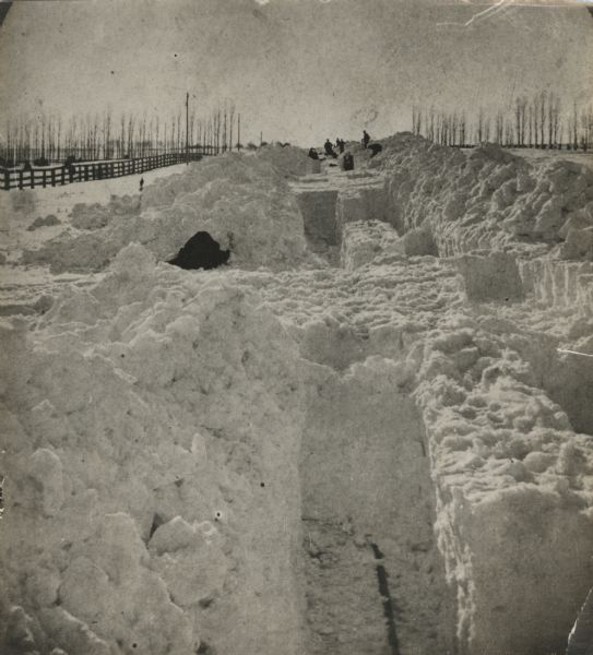 A winter scene with men digging out the train tracks by hand after a big snow storm in Racine County. Trees and a fence line the sides of the railroad right of way. Hand written on reverse: "The great snow fall." Between February 27th and March 4th, 1881, 2 to 4 feet fell in eastern and central Wisconsin with drifts up to 20 feet.