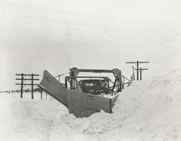 Winter scene with man driving a Model RD-8 La Plant-Choate V-Plow Snow Plow with side extension blades from the front. In the background are power poles.