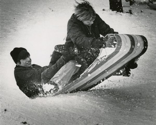 Winter scene with teenage toboggan riders, Rick Borckel (age 14) and Pat Voight (age 13), hitting a bump on a hill in Brown Deer Park, Milwaukee.