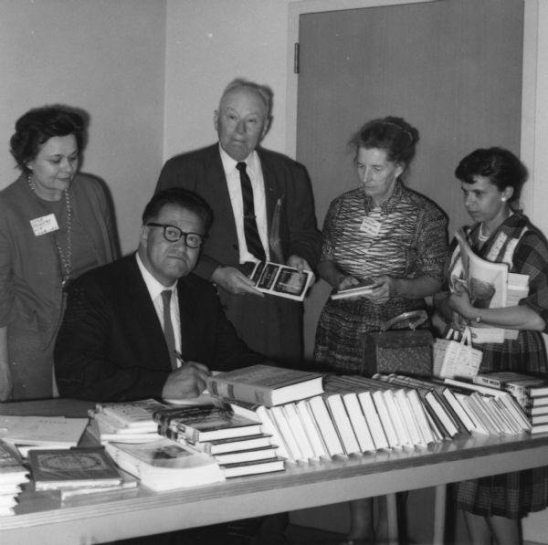 August Derleth (seated) signs books at a meeting of the Wisconsin Fellowship of Poets. Behind him are (l to r): Star Powers, Marvin Davis Winsett, Mildred Breedlove and Jo Bartels Alderson.