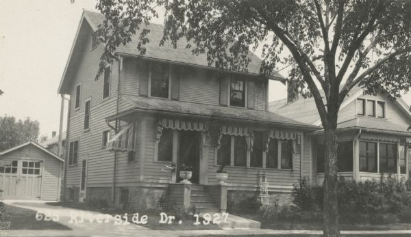 Photographic postcard view from street of the house at 625 Riverside Drive. In the front is an enclosed porch with awnings over the windows. Caption reads: "625 Riverside Dr. 1927."