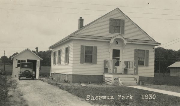 Photographic postcard view of the house at 1610 Sheridan Drive, built by Willard Droster, in the Sherman Park neighborhood. A car is parked in the driveway outside the garage behind the house on the left.