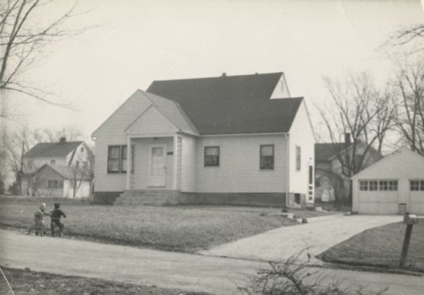 View across street towards the house at 1717 Fremont Avenue. Two small children are riding tricycles in front of the house.