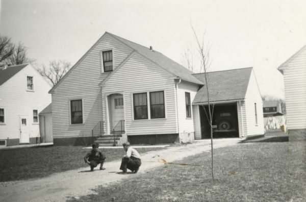 Exterior view of house at 1513 Hooker Avenue. Two children are playing in the driveway. The garage door is open and an automobile is parked inside. The house was built by Willard Droster.