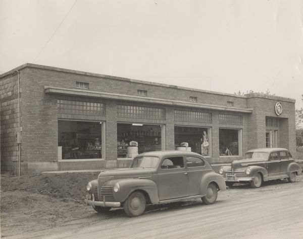 Exterior of the Ridgeway Lumber Store before the opening on May 15, 1948. Two cars are parked in front, and merchandise can be seen in the large show windows. There is a clock over the entrance on the right. Owned by Elmer and Willard Droster, and G. Wichman.