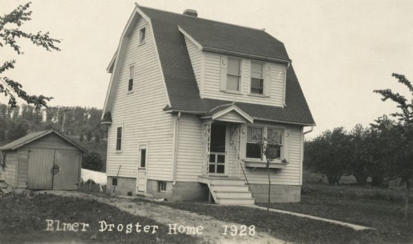 Exterior view of the Elmer Droster home at 5301 Felland Road. There is a garage on the left, and in the far background a ridge with trees.