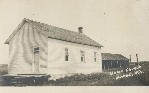 Photographic postcard view of Burke Union Church on Felland Road. Behind the building on the right is a shed. The church was torn down in the 1920s. This building used to be the Grange, which was located on Nelson Road, and moved about 1890. Caption reads: "Union Church, Burke, Wis."