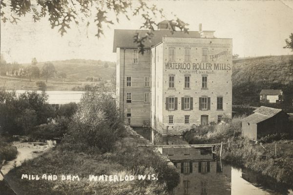 Photographic postcard of an elevated view looking down at the Waterloo Roller Mills and Dam. Caption reads: "Mill and Dam, Waterloo, Wis."