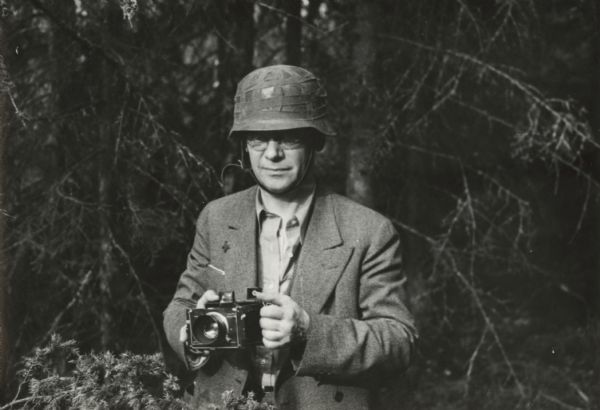 Louis Lochner standing outdoors holding a camera. He is wearing a helmet.