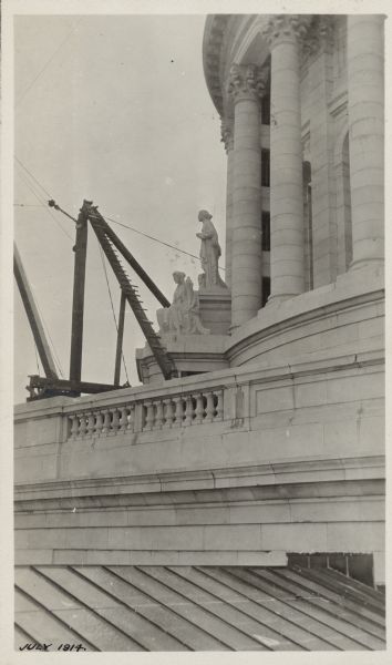 Scaffold used to hoist the statue "Wisconsin" to the Capitol dome is set up near two stone statues above a stone balcony.