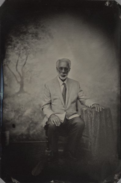 Modern tintype, full length, formal portrait, of Ellsworth H. Brown, Ph.D., The Ruth and Hartley Barker Director, Wisconsin Historical Foundation. Development Officer, Wisconsin Historical Foundation. He is seated in a chair with his arm resting on a table, in the background is a painted backdrop.
