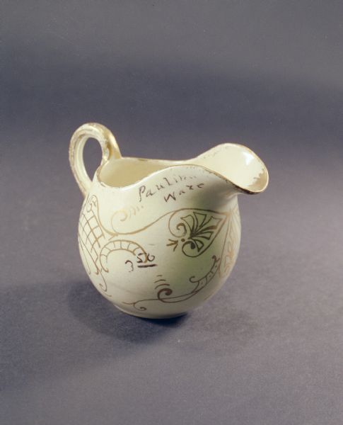 Pauline pottery pitcher in white decorated with gold. Near the lip of the pitcher are the words: "Pauline Ware."