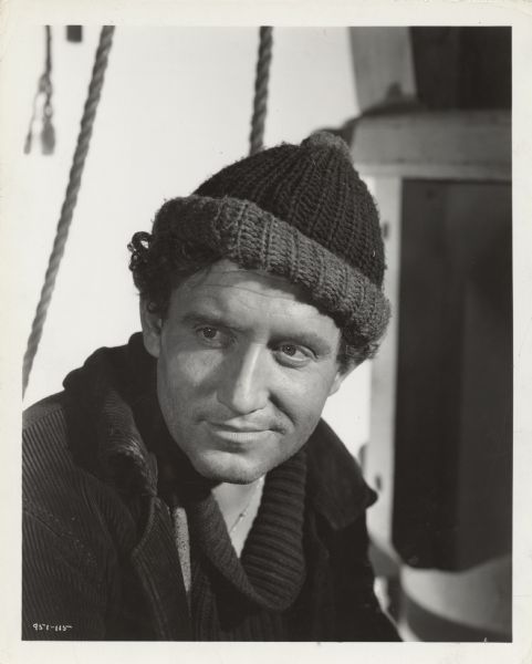 Publicity photograph of Spencer Tracy as Manuel in the film <i>Captains Courageous<i>. He is wearing a knit stocking cap and corduroy coat.
 	