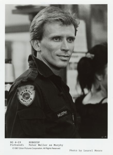 Portrait of Peter Weller as Murphy in the movie <i>Robocop</i>. He is wearing a jacket with a Detroit Police department patch on the shoulder.
