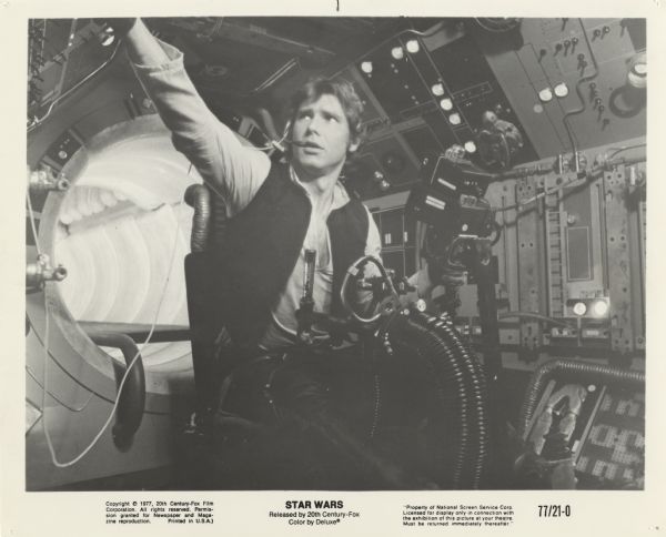 Still photo of Harrison Ford, as Han Solo, preparing to fire one of the Millenium Falcon's weapons in the film <i>Star Wars</i>.