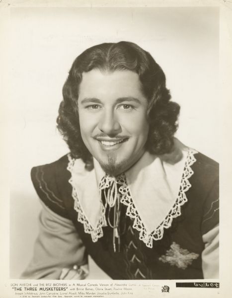 Publicity photograph of Don Ameche in character as D'Artagnan in <i>The Three Musketeers</i>. He has long hair, a thin mustache and goatee. The costume includes a large white collar.