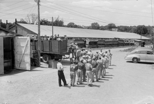 Elevated view of a work shift of German prisoners at a prisoner of war camp marching to a truck to be conveyed to work at a local cannery.