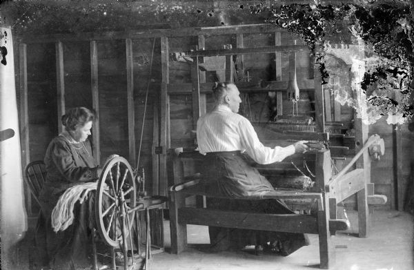 Mrs. (Christine) Peterson and Mrs. Torgeson (a neighbor) are working in the upstairs loft of the barn. Christine is sitting in a chair using a spinning wheel. Mrs. Torgeson is weaving on a large loom. Quote from the book <i>A Life in Photographs and Letters, Carl & Christine Peterson, My Grandparents</i>, "Christine was always a hard worker, expert gardener and seamstress. She would buy wool, have it carded and then spin it. She made all their clothing, including very scratchy undergarments for winter."