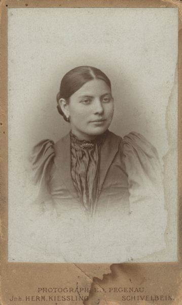 Waist-up vignetted formal studio carte-de-visite of Anna Bielke (later Ott). She is wearing a dress with a collar pin, and earrings. At the bottom of the card is the name of the photographic studio, photographer and location, "Photograph: Ed. Pegenau. Jnh. Herm. Kiessling. Schivelbein." Translated: Photographer: Ed. Pegenau, John Herman Kiessling. Schivelbein, Germany, (now Swidwin, Poland.)