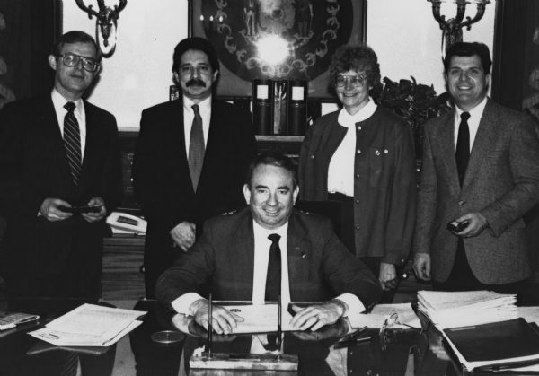Mayor Paul Soglin posing in a group portrait with Governor Tommy Thompson (sitting at his desk). Standing in a row behind the Governor is, (l to r): David Prosser, Paul Soglin, Rebecca Young and (may be Edward J.) Huck.