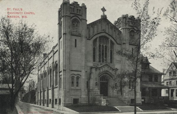 View from State Street looking towards St. Paul's University Chapel, 723 State Street. Text on postcard reads: "St. Paul's University Chapel, Madison, Wis., E.C. Kropp Co. Milwaukee." There are wood buildings next to the church on the right. Fitch Court runs along the left side of the building towards University Avenue.