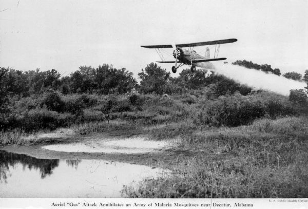View of a crop duster spraying a pesticide to control Malaria mosquitoes over a pond. The caption under the image reads: "Aerial 'Gas' Attack Annihilates an Army of Malaria Mosquitoes near Decatur, Alabama."