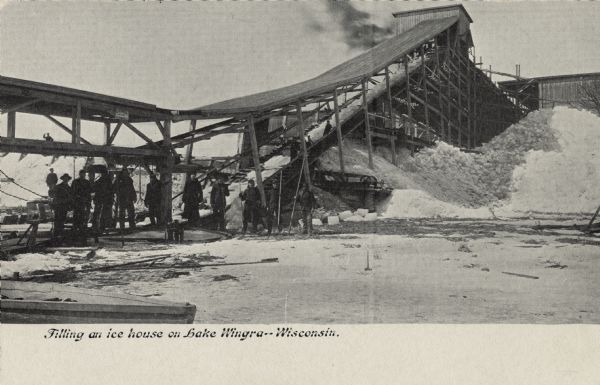 Caption reads: "Filling an ice house on Lake Wingra--Wisconsin." A large scaffold holds up the conveyor into the ice house, and a group of men are standing under the conveyor structure. Piles of ice are on the right and left.