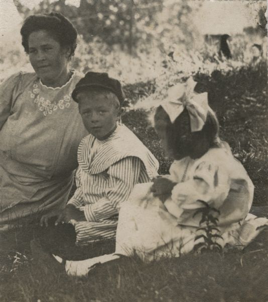 Christine (mother), Laurie and Muriel Peterson sitting in the grass. Laurie is looking directly at the camera.