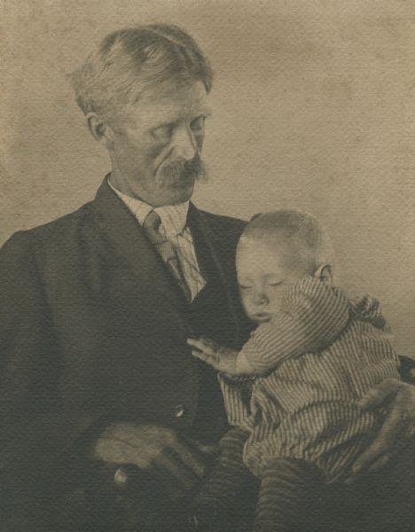 Waist-up portrait of Carl Peterson with his youngest child, James, asleep on his lap.