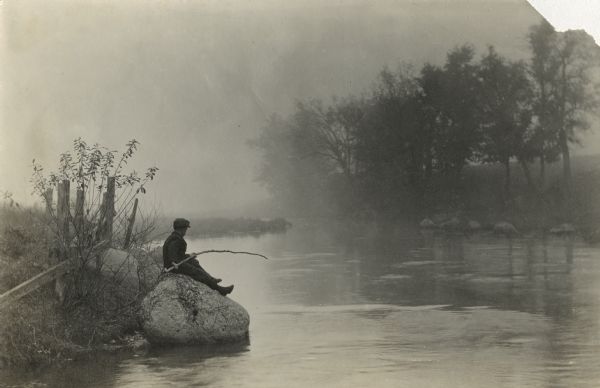 View across water towards Laurie Peterson, son of the photographer, fishing from a rock on a misty morning near the family home.