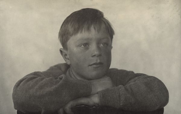 Quarter-length portrait of Laurie Peterson posing with his arms folded over the back of a chair, resting his chin on his hands.