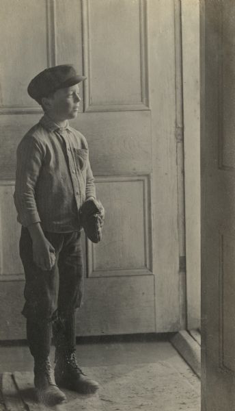 Laurie Peterson standing indoors gazing through an open doorway, and holding a baseball and baseball glove.