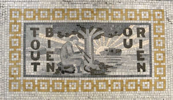 Mosaic in the central lobby floor of the Wisconsin Historical Society, near the statue "Forward." This is the printer's mark of the Riverside Press. It was chosen to represent American printers. The design is by Elihu Vedder, modified by the architects for mosaic treatment. The French text on the mosaic translates as "All Good or Nothing."
