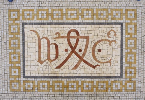 Mosaic in the central lobby floor of the Wisconsin Historical Society. This is the printer's mark of one the earliest English printers, William Caxton. He designed his mark in 1489. The initials "W" and "C" flank a symbol usually interpreted as the number "74," possibly referring to 1474, when printing was introduced into England.<p>The design between the initials "WC" is thought to reproduce a merchant’s mark he used before becoming a printer.</p>