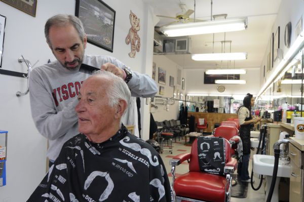 The last week of business at the College Barber Shop. The owner Larry Cobb is cutting employee Don Fine's hair. In the background is a female stylist.