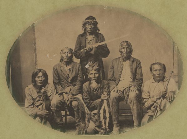 Group of Ho Chunk Indians that visited Governor Lucius Fairchild. Names, (standing), Dandy, holding a long stemmed pipe, (Four-Leg's son), (seated) Wau-So-Mo-Ne-Ka (Hail-stone) has a skunk skin over his knee and his brother, Yellow Thunder, (kneeling) Nes-Ka-Ka (Whitewater), Spoon-De-Kaury (son of Scha-Chip-Ka-Ka) holding a skunk skin, and Chou-Ga-Ga (grandson of Scha-Chip-Ka-Ka) holding a stick.