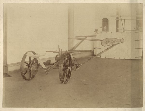 Indoor view of a horse-drawn McCormick Mower. Wheels and writing suggest an early model predating International Harvester's 1903 incorporation.