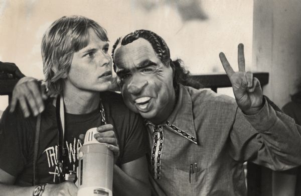 A person wearing a Richard Nixon mask and flashing a peace sign is posing with Michael Kienitz, who is holding a megaphone and wearing a t-shirt advertising the film, "The War at Home."<p>Note from Michael Kienitz, "While creating sound effects at Orton Park for the <i>The War at Home</i> in 1979, President Nixon visited us."</p>