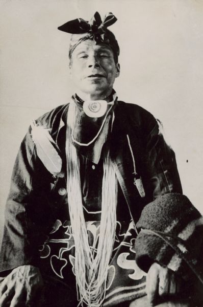 An Algonquin Ojibwa man dressed in traditional Native American clothing, with a blanket over his arm.