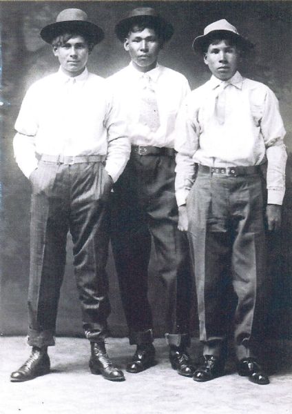 Three young Native American men pose for a studio portrait. Joseph Oiyette (White Earth Tribe) is on the right, the other two student's names are unknown. They attended the Carlisle Boarding School in the late 1910s.